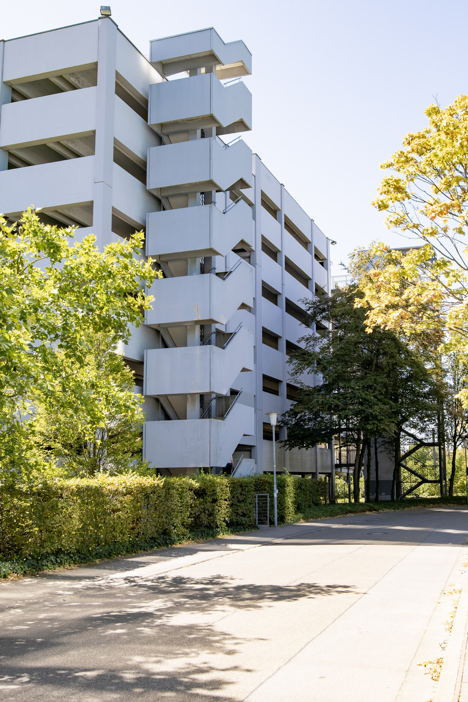 Modernes Parkhausgebäude und Bäumen im Vordergrund, sonniger Tag.