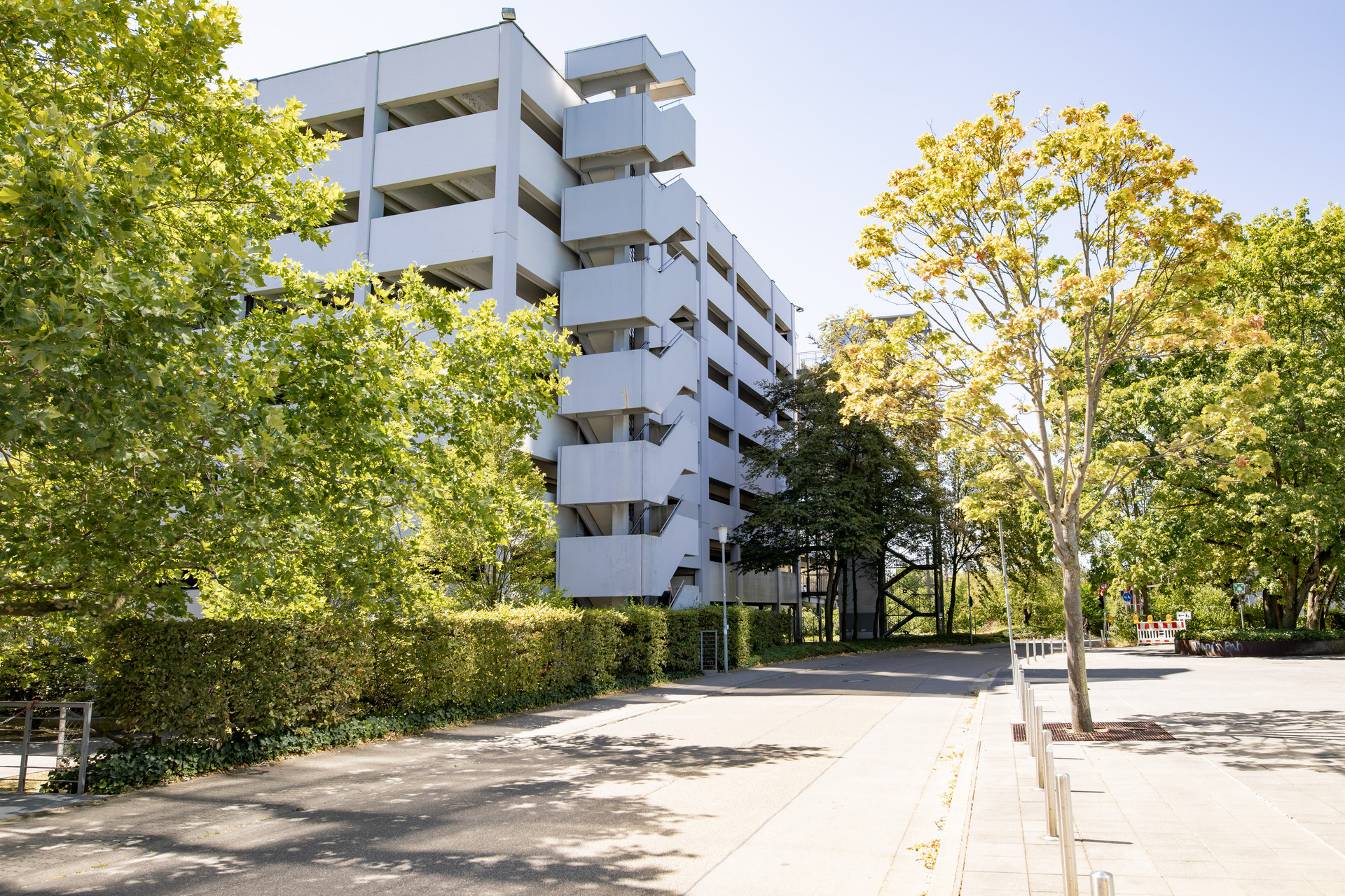 Modernes Parkhausgebäude und Bäumen im Vordergrund, sonniger Tag.
