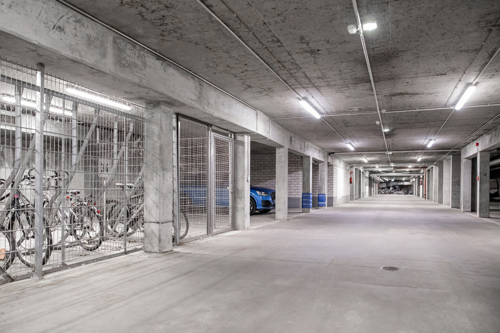 Unterirdischer Parkhausgang mit Fahrradständern, Fahrrädern und einem geparkten Auto, beleuchtet und mit Betonwänden.
