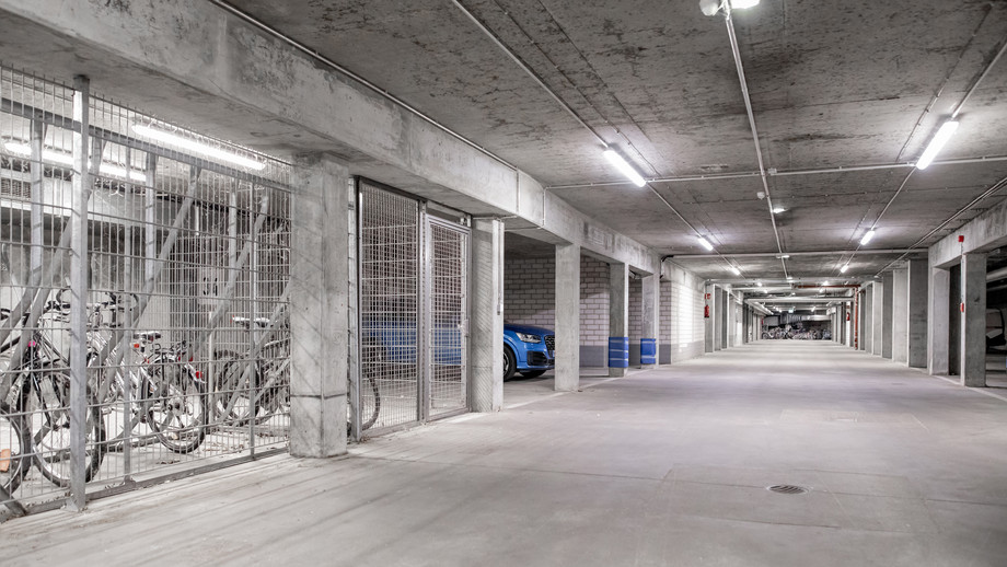 Unterirdischer Parkhausgang mit Fahrradständern, Fahrrädern und einem geparkten Auto, beleuchtet und mit Betonwänden.