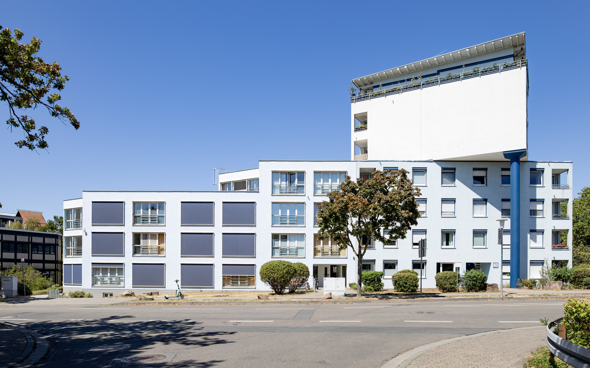 Moderne Mehrfamilienhausanlage mit hellen Fassaden, Balkonen und Bäumen vor dem Gebäude, ruhige Straßenansicht.