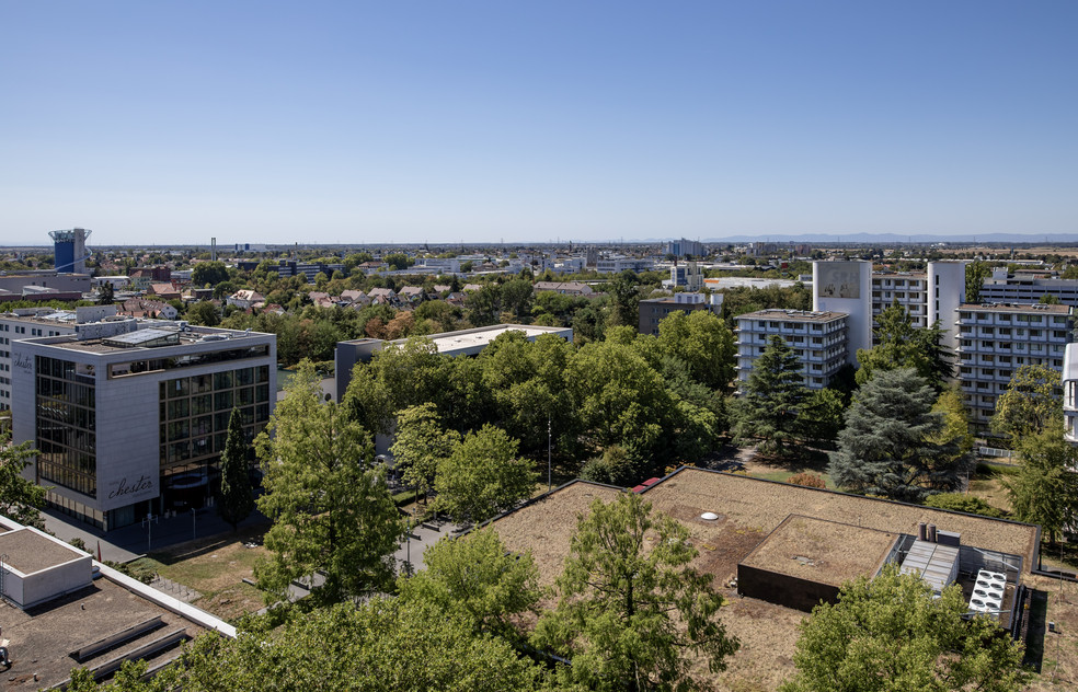 Luftbild einer Stadt mit Gebäuden, Grünflächen und Fernsicht zu weiteren Wohnhäusern und Industrieanlagen.