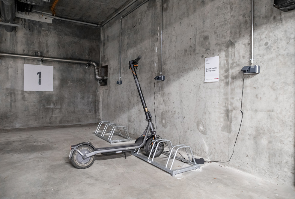 Ein Elektro-Roller im Parkhaus mit Ladekabel und Ladestation an der Wand. Nummer 1 markiert an der Betonwand.